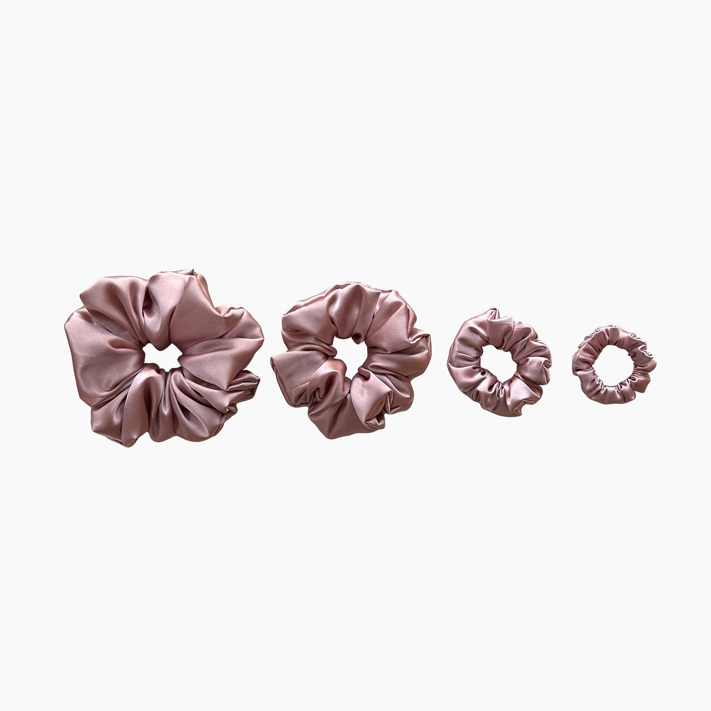 Set of four pink satin scrunchies from Nude collection in varying sizes like mini, small, medium and large, displayed in a row on a white background.