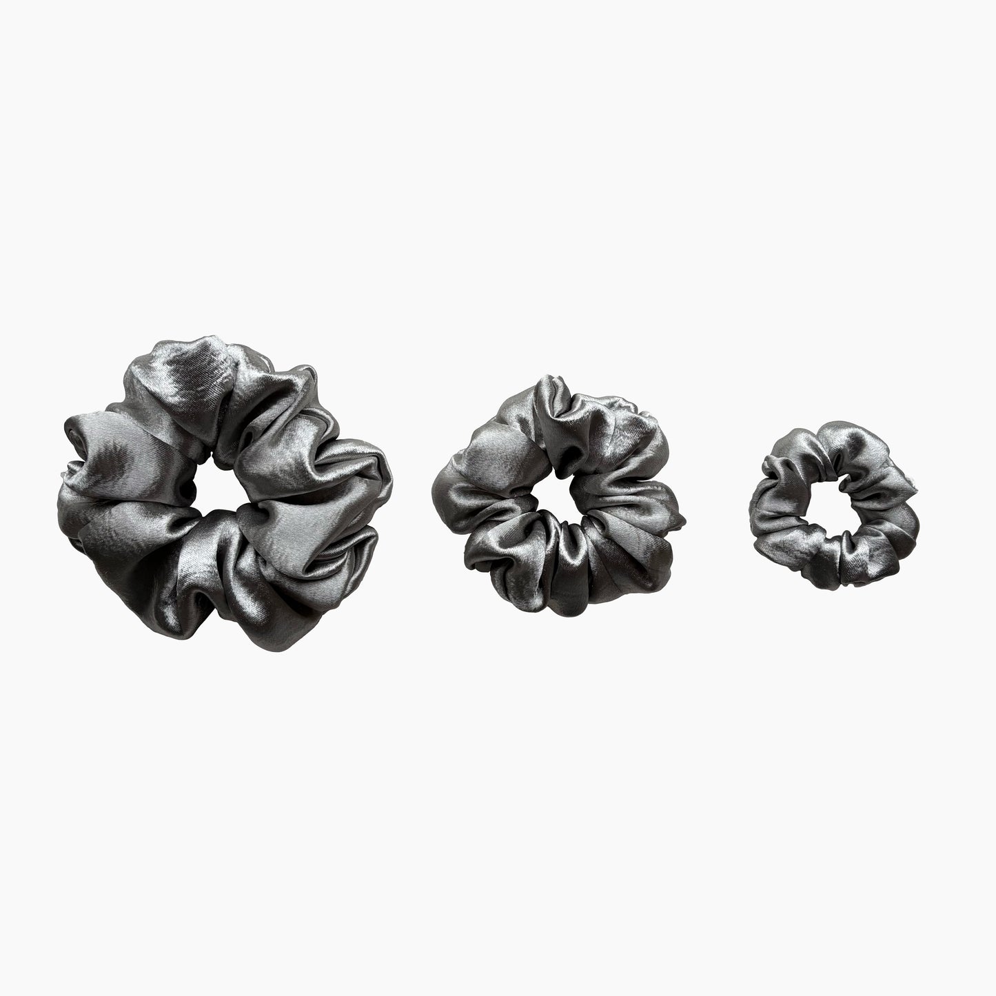 Set of tree silver satin scrunchies from Pebble Satin collection in varying sizes like small, medium and large, displayed in a row on a white background.