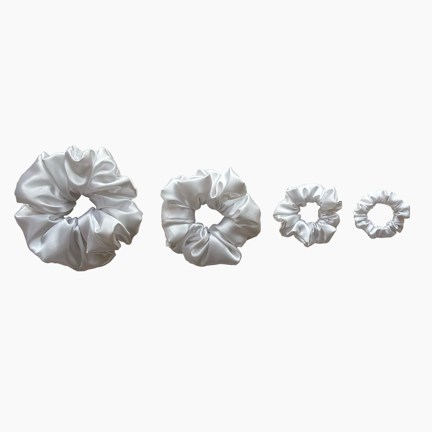 Set of four white satin scrunchies from Nude collection in varying sizes like mini, small, medium and large, displayed in a row on a white background.