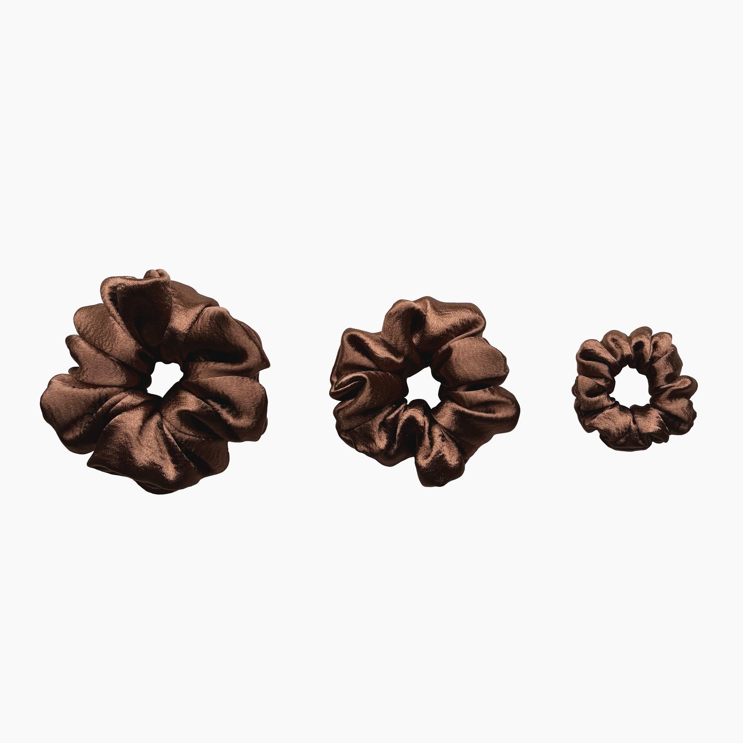 Set of tree mocha mousse satin scrunchies from Pebble Satin collection in varying sizes like small, medium and large, displayed in a row on a white background.