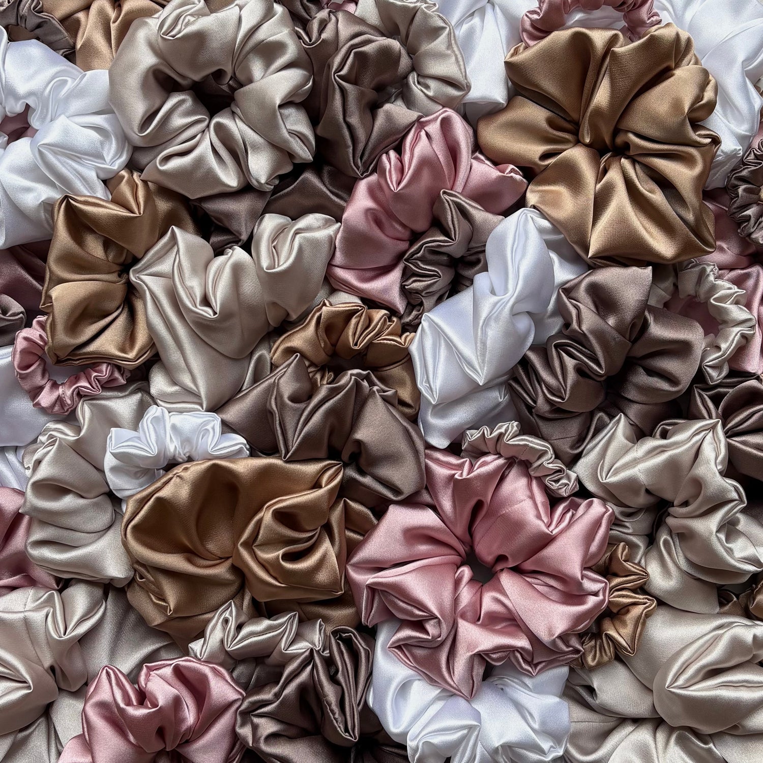 Assorted satin scrunchies in mini, small, medium, and large sizes, featuring nude tones like pink, white, beige, gold and brown.