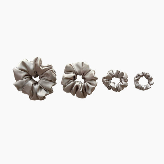 Set of four beige satin scrunchies from Nude collection in varying sizes like mini, small, medium and large, displayed in a row on a white background.