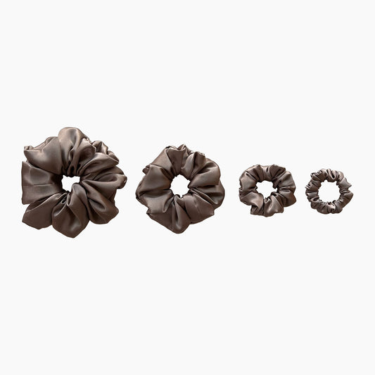 Set of four brown satin scrunchies from Nude collection in varying sizes like mini, small, medium and large, displayed in a row on a white background.