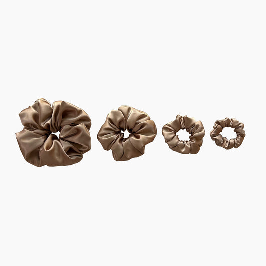Set of four gold satin scrunchies from Nude collection in varying sizes like mini, small, medium and large, displayed in a row on a white background.