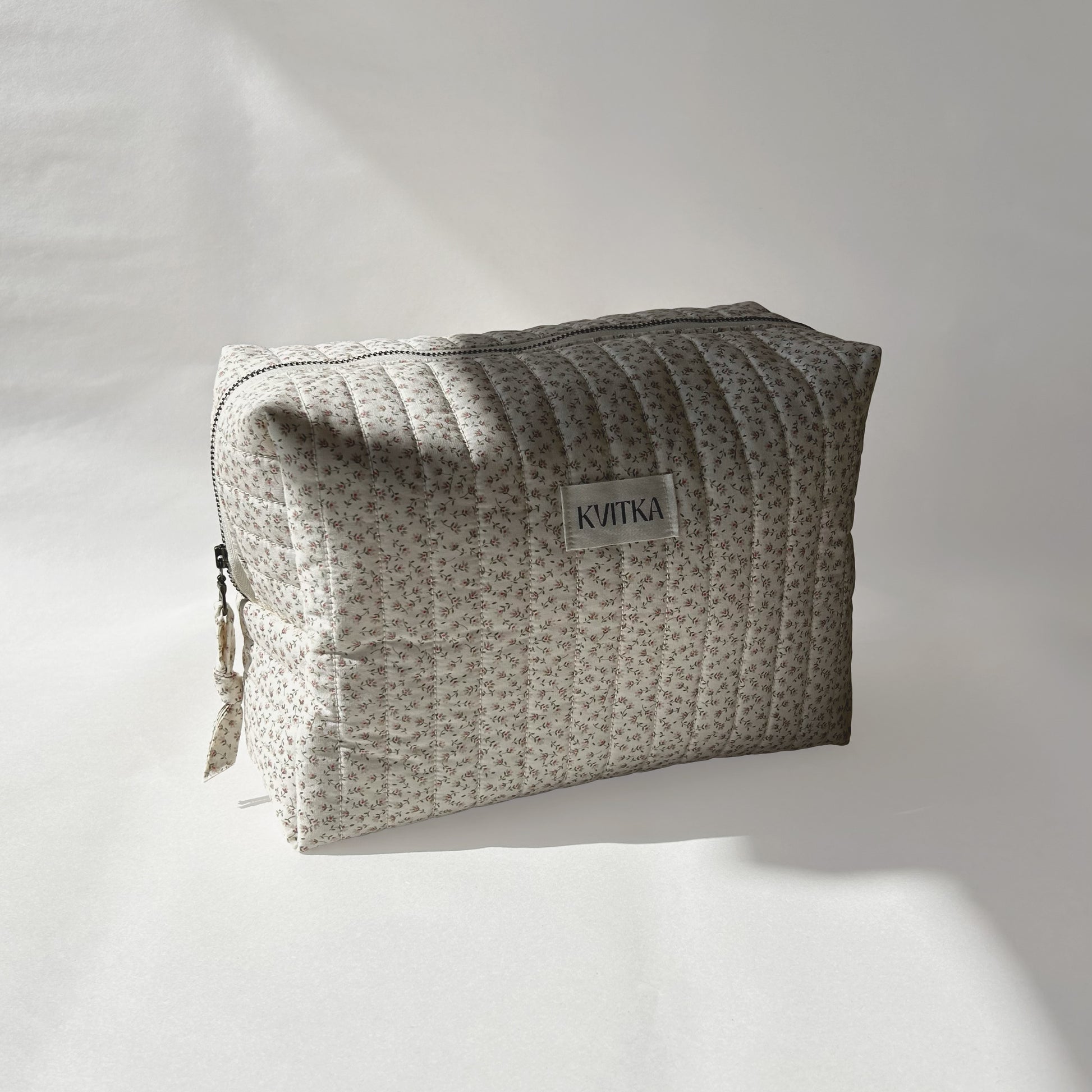 Large-size of quilted makeup bag from the Ditsy Blossom collection, angled to the left view to display zip with a zip pull, on a soft white background.