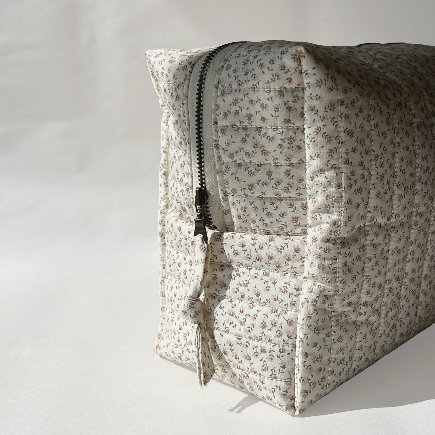Large-size of quilted makeup bag from the Ditsy Blossom collection, angled to the left view to display zip with a zip pull, on a soft white background.