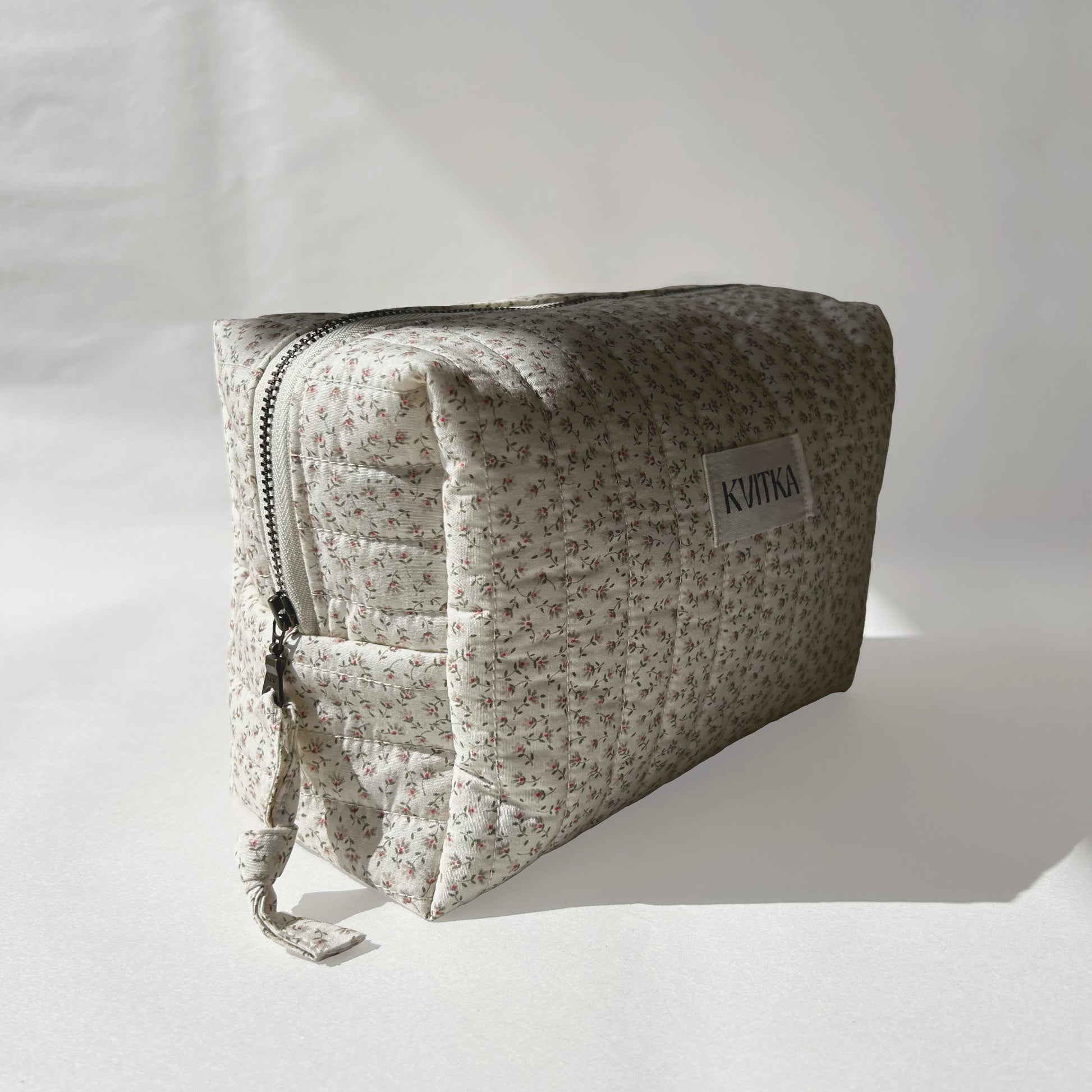 Medium-size of quilted makeup bag from the Ditsy Blossom collection, angled to the left view to display zip with a zip pull, on a soft white background.
