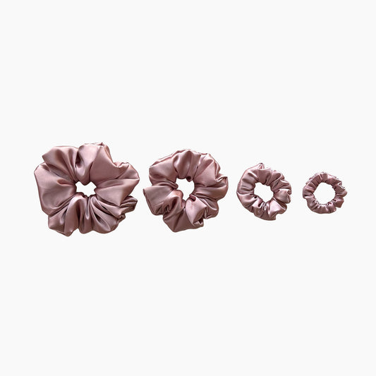 Set of four pink satin scrunchies from Nude collection in varying sizes like mini, small, medium and large, displayed in a row on a white background.