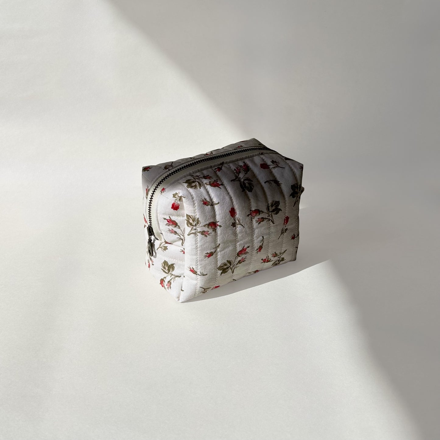 Mini-size of quilted makeup bag from the Bell Pivoines collection, angled to the left view to display zip on a soft white background.