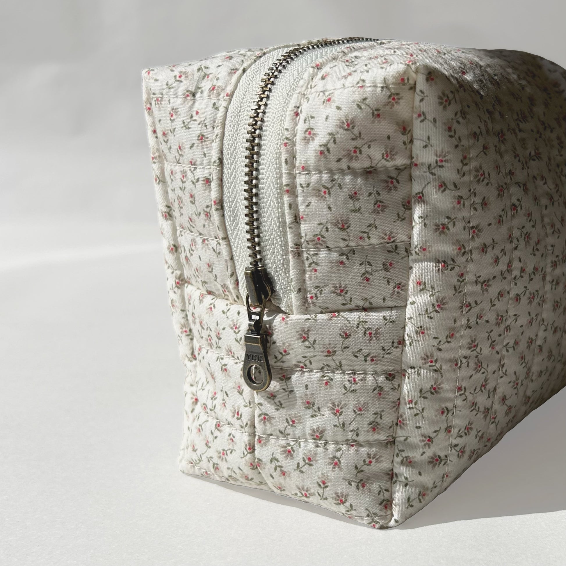 Mini-size of quilted makeup bag from the Ditsy Blossom collection, angled to the left view to display zip, on a soft white background.