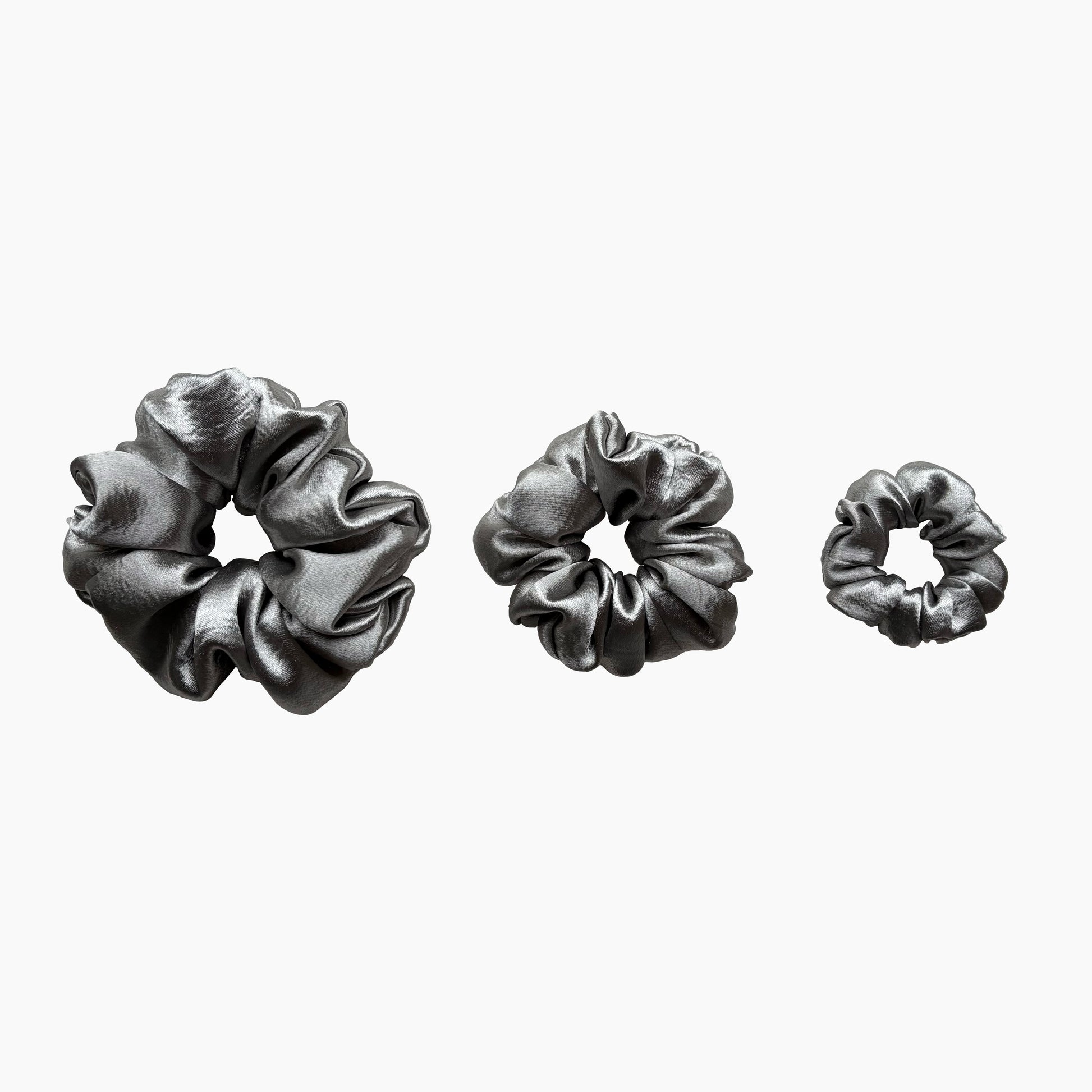 Set of tree silver satin scrunchies from Pebble Satin collection in varying sizes like small, medium and large, displayed in a row on a white background.