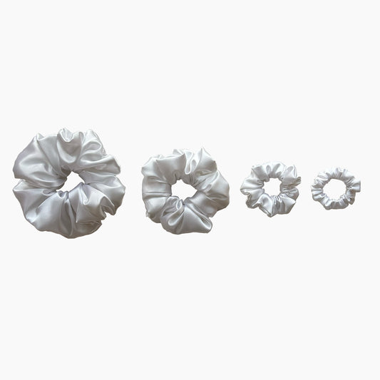 Set of four white satin scrunchies from Nude collection in varying sizes like mini, small, medium and large, displayed in a row on a white background.
