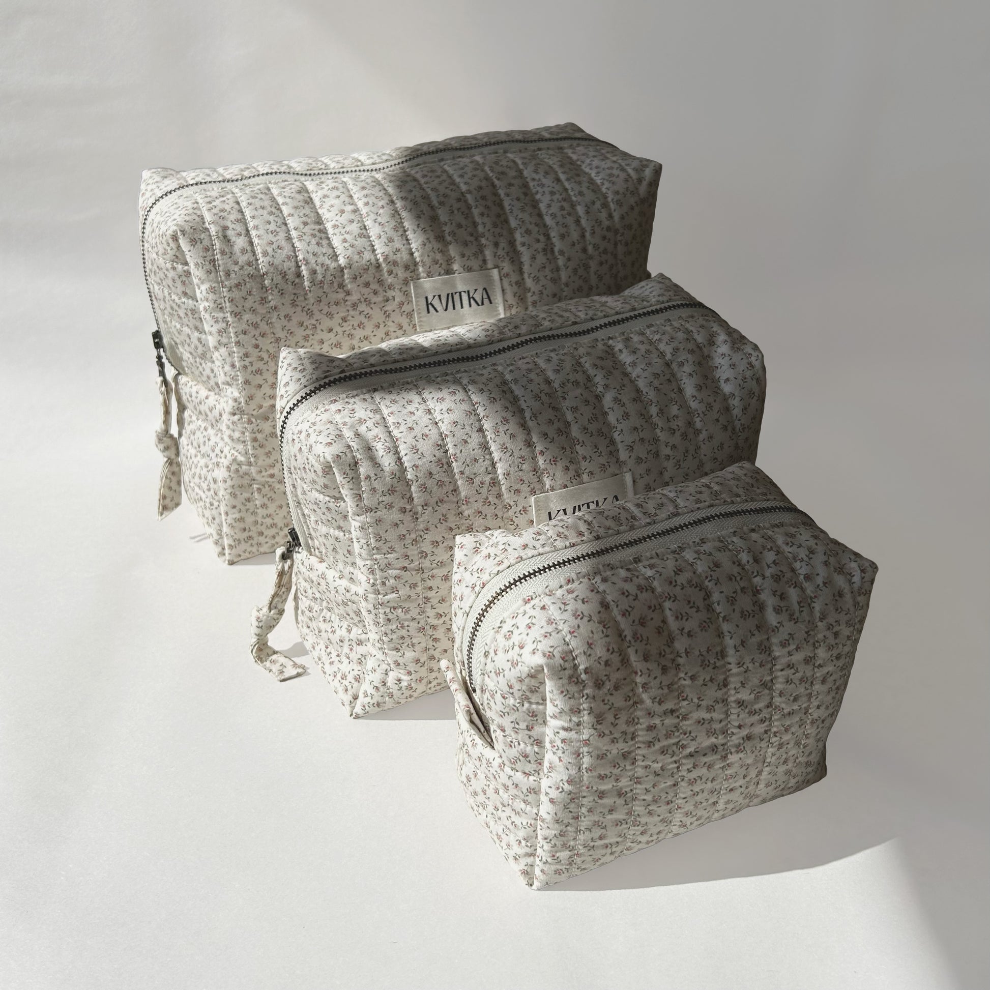 Angled to the left view of Ditsy Blossom quilted makeup bags collection in three sizes - mini, medium, and large sizes, arranged from front to back on a soft white background.