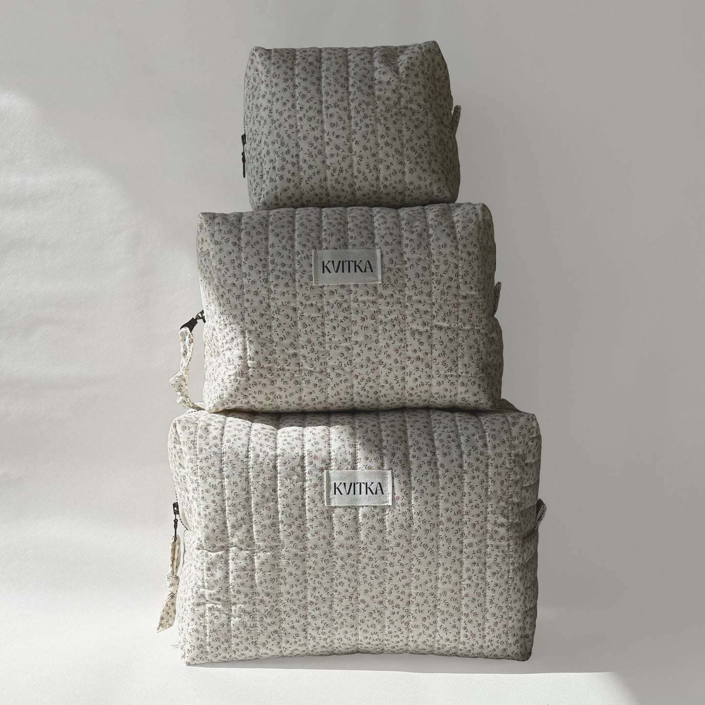 Set of three quilted makeup bags from the Ditsy Blossom collection, shown in mini, medium, and large sizes, displayed on top of each other for size comparison on a soft white background.