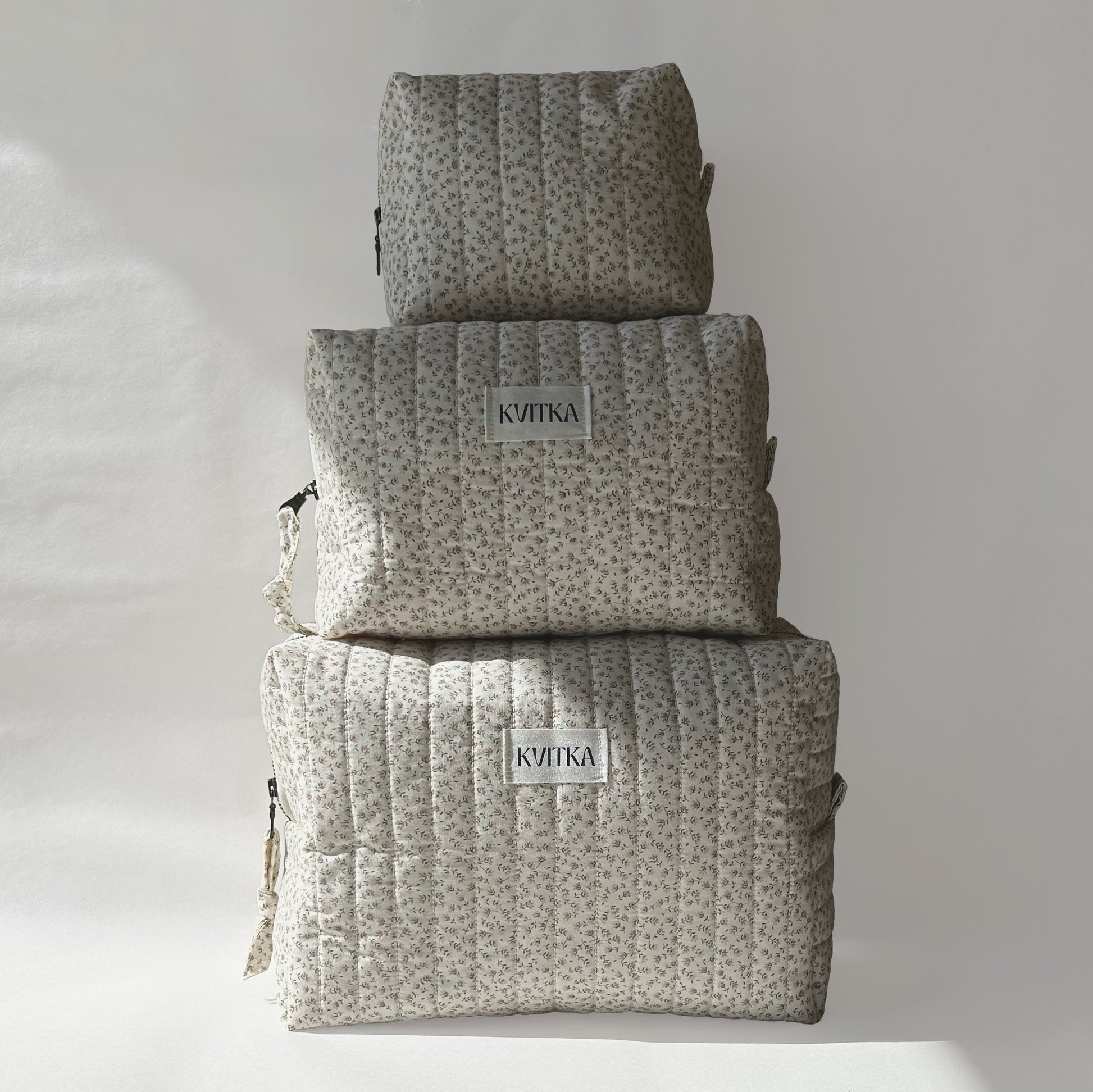 Set of three quilted makeup bags from the Ditsy Blossom collection, shown in mini, medium, and large sizes, displayed on top of each other for size comparison on a soft white background.