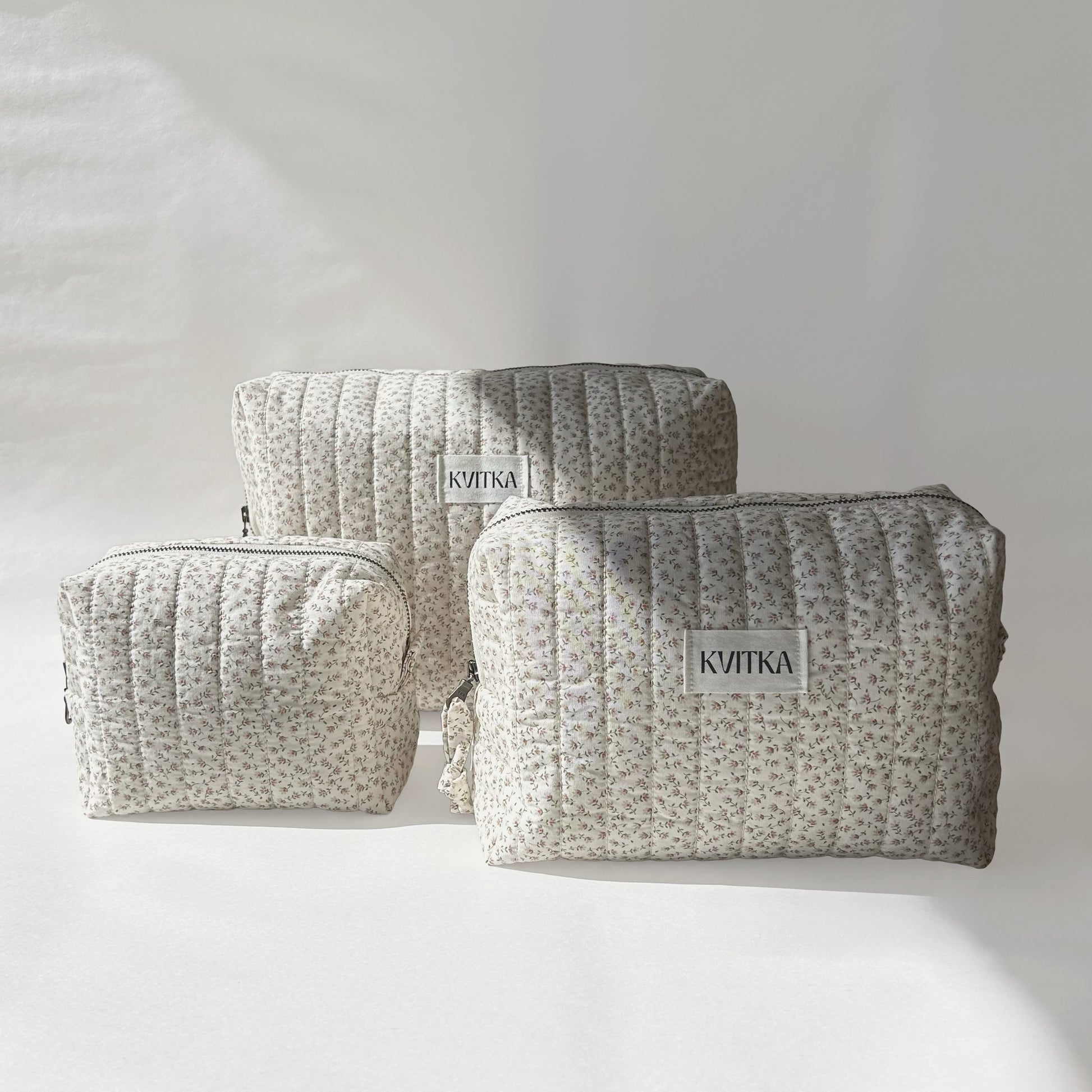 Front-facing view of Ditsy Blossom quilted makeup bags collection in three sizes - mini, medium, and large on a soft white background.