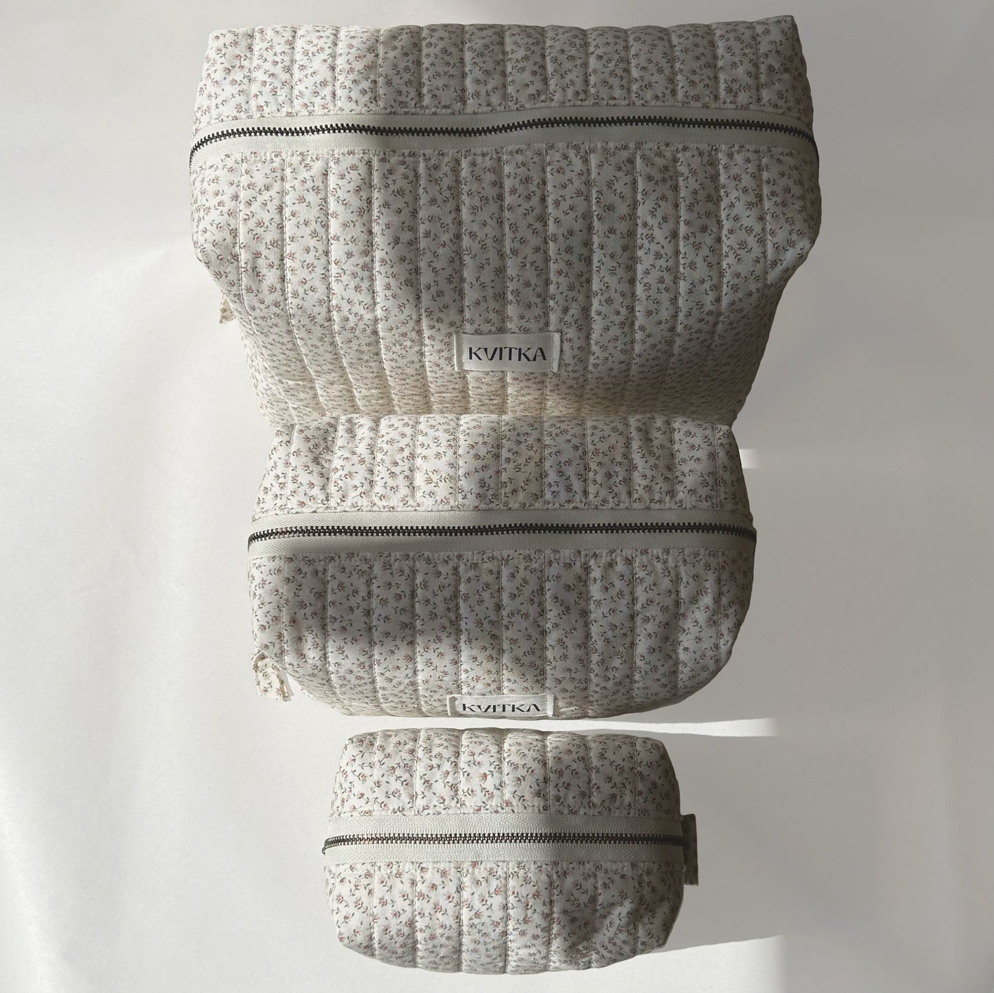Top view of Ditsy Blossom quilted makeup bags collection in three sizes - mini, medium, and large arranged from front to back on a soft white background.