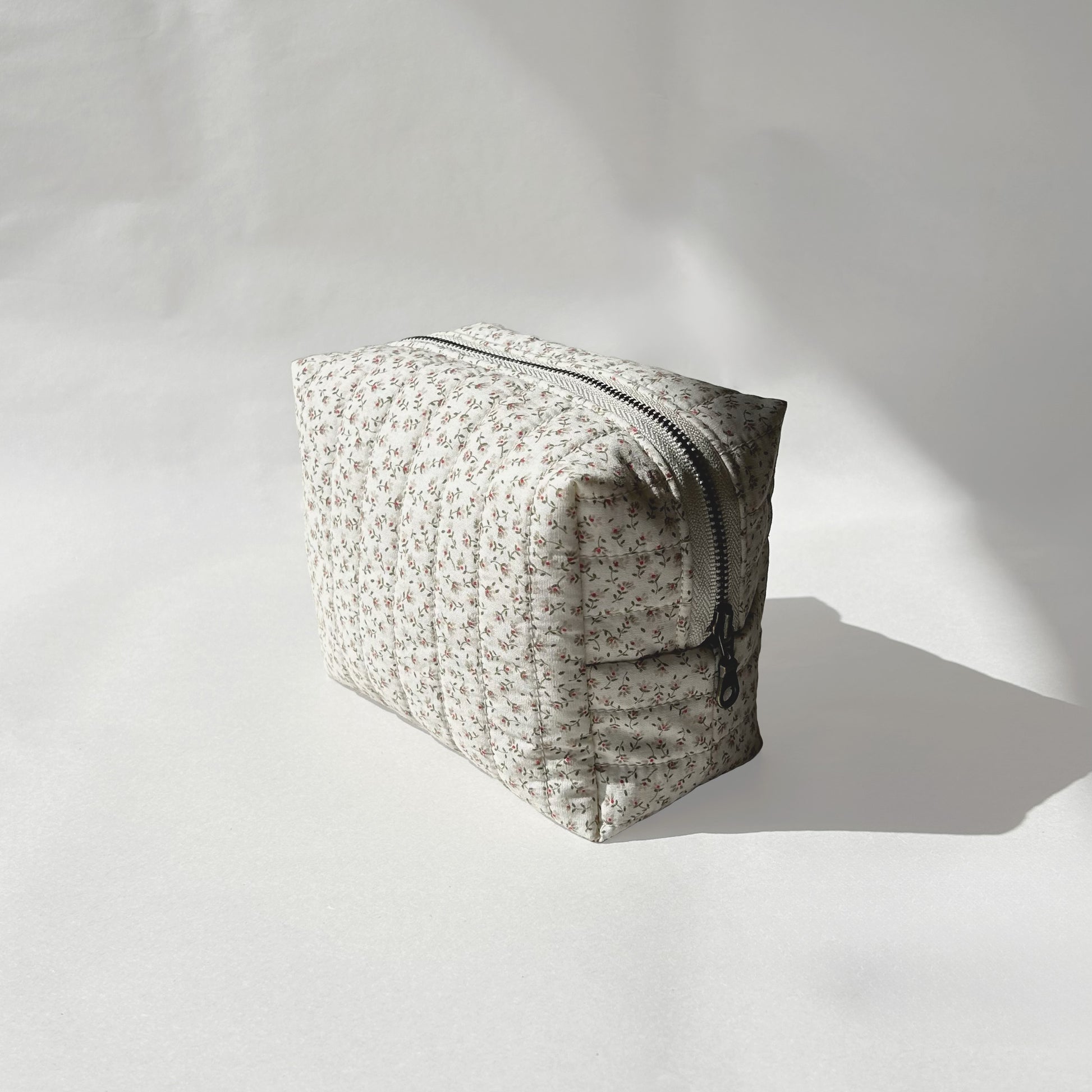 Mini-size of quilted makeup bag from the Ditsy Blossom collection, angled to the right view to display zip on a soft white background.